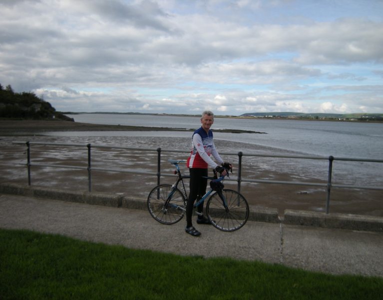 Photo of the host for our cycling holidays and walking tours of Devon and Cornwall, Ian - pictured here on his bicycle on a road beside the sea