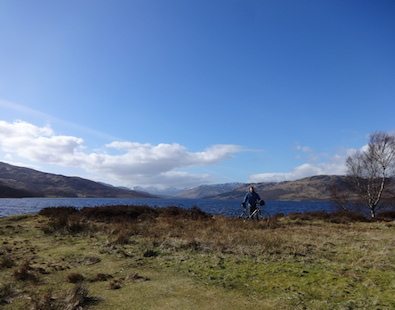 One of The Carter Company team members standing with his bike, with Loch Katrine and mountains in the background